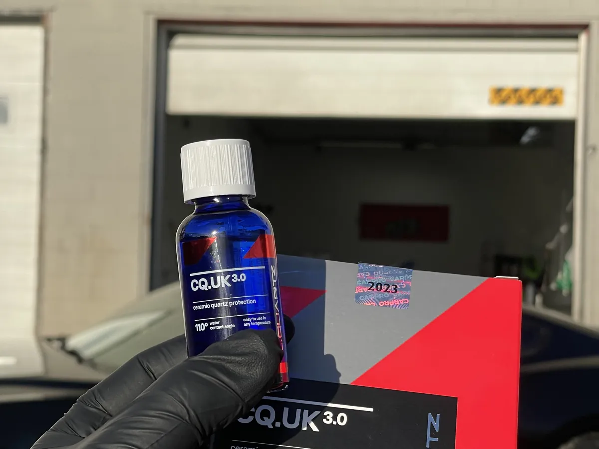 Technician holding a CQuartz ceramic coating kit in front of a black car